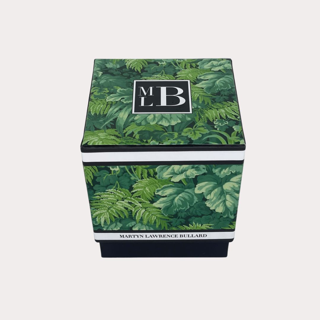 Martyn Lawrence Bullard Signature Extraordinaire candle in clear glass jar with black and white MLB label, lit and styled on a coffee table with design books and modern art