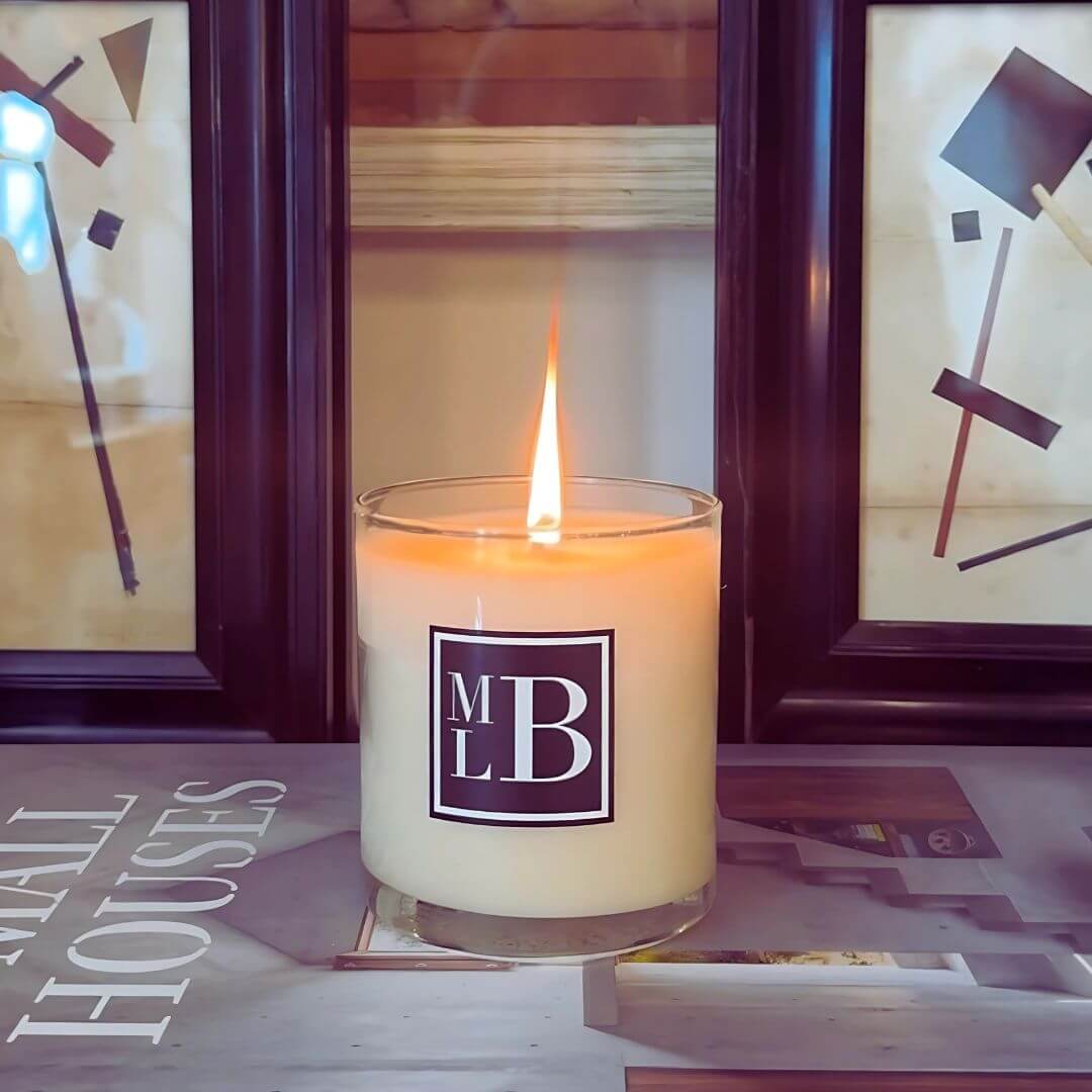 Martyn Lawrence Bullard candle in clear glass jar with black and white MLB label, lit and styled on a coffee table with design books and modern art